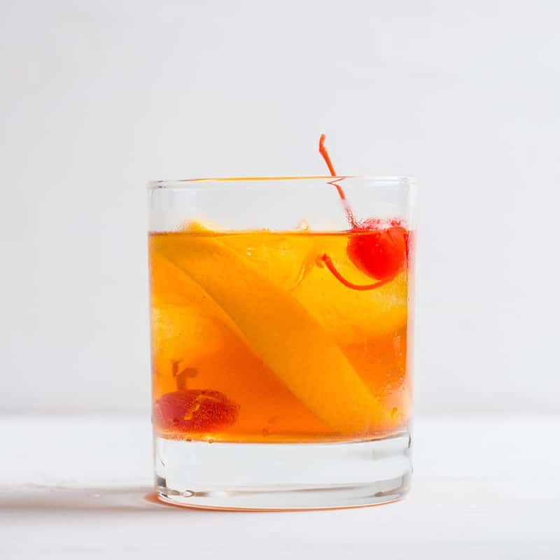 Glas mit Old Fashioned Longdrink, mit einer Zitronenzeste und einer Kirsche